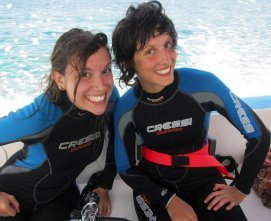 Two girls on a boat wearing wetsuits smiling