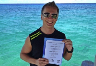 Student diver proudly shonwing his certificate of completion at the shore