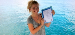 Proud open water diver graduate showing her certificate standing on a dock